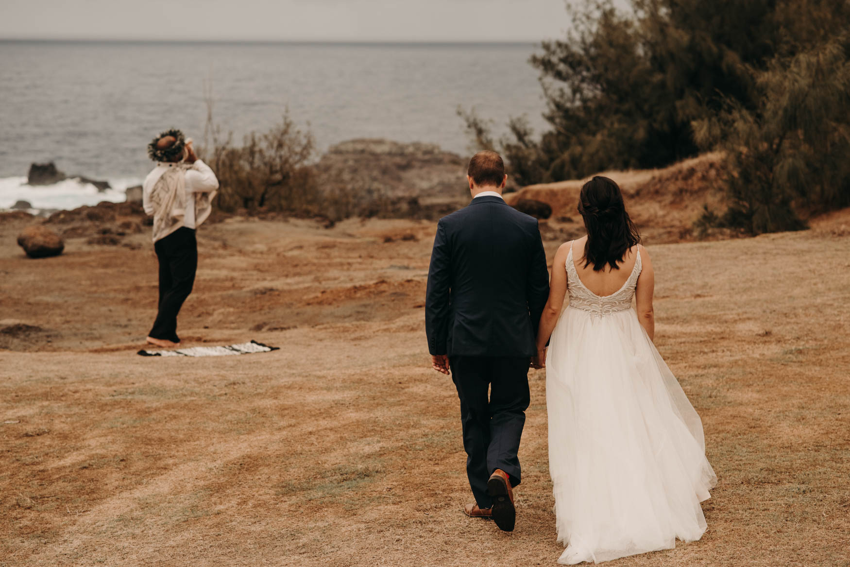 While Euta blows the conch toward the ocean, Andrew and Alison walk into frame holding hands.